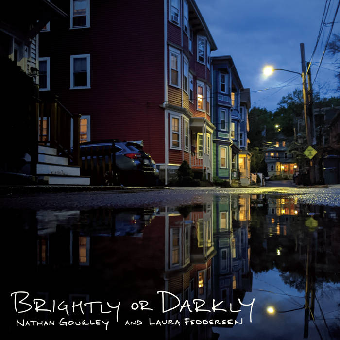 A photo of a row of homes illuminated on the front by a street light and dark on the side. The homes are reflected in a puddle in the street.