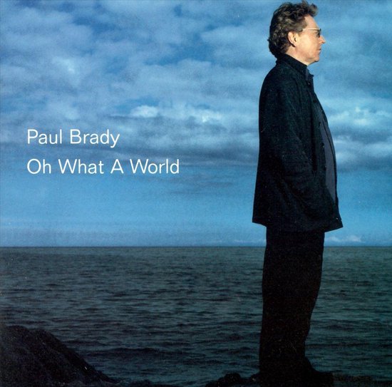 Album cover with a person standing on a cliff overlooking the ocean, featuring the text 'Paul Brady Oh What A World'.