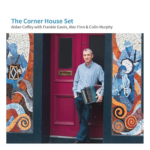 A man stands in a doorway holding a button accordion at his side
